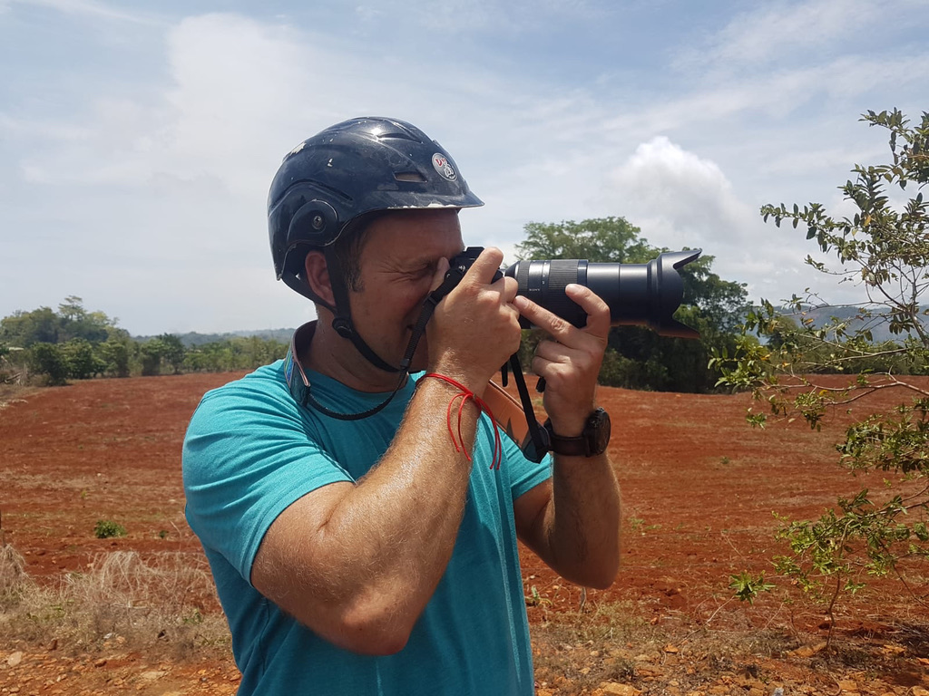 Birk Möbius fotografiert mit Helm und Kamera vor roter Erde