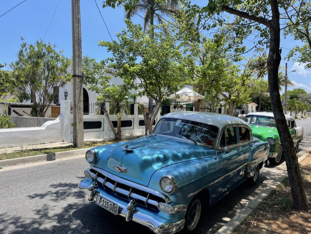 Türkisblauer Oldtimer im Schatten von Bäumen auf Kuba