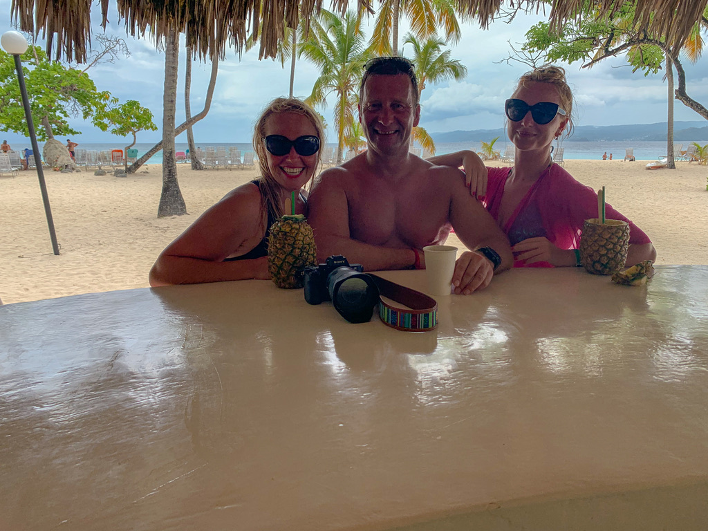 Birk Möbius mit zwei Mitreisenden an einer Strandbar unter Palmblättern