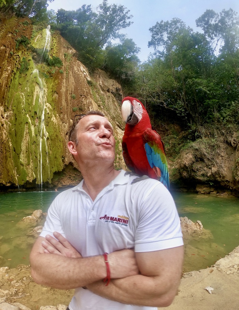 Birk Möbius mit einem roten Ara auf der Schulter vor einem Wasserfall